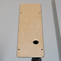 Tan MDF zero clearance insert for Bosch GTS18 table saw, viewed from above, with four mounting holes and central blade opening