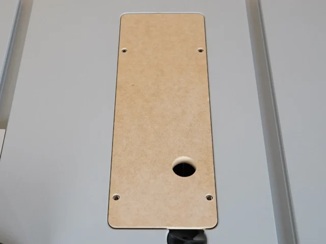 Tan MDF zero clearance insert for Bosch GTS18 table saw, viewed from above, with four mounting holes and central blade opening