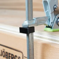 Black stop block clipped onto vertical rail of Festool track saw, with green-base clamp holder visible in background on MFT table