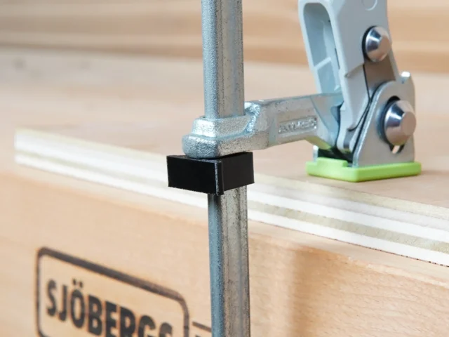 Black stop block clipped onto vertical rail of Festool track saw, with green-base clamp holder visible in background on MFT table