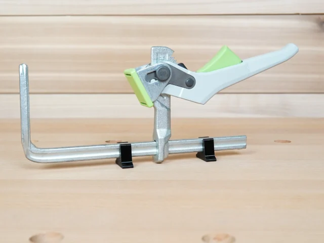 Set of stop blocks mounted on a metal quick clamp bar, with black stands supporting the rail and lime-green and light blue blocks limiting clamp travel