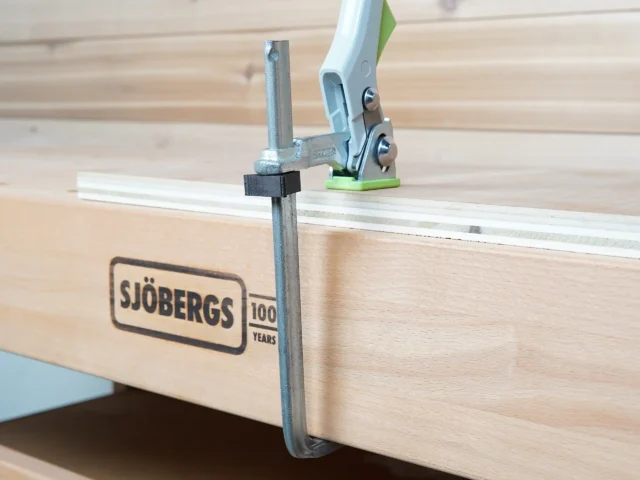 Black stop block mounted on metal shaft of Bessey quick clamp clamped to Sjöbergs MFT workbench