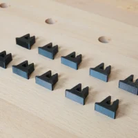 Ten black and blue 3D-printed stop blocks arranged on a light wood surface with pocket holes visible above