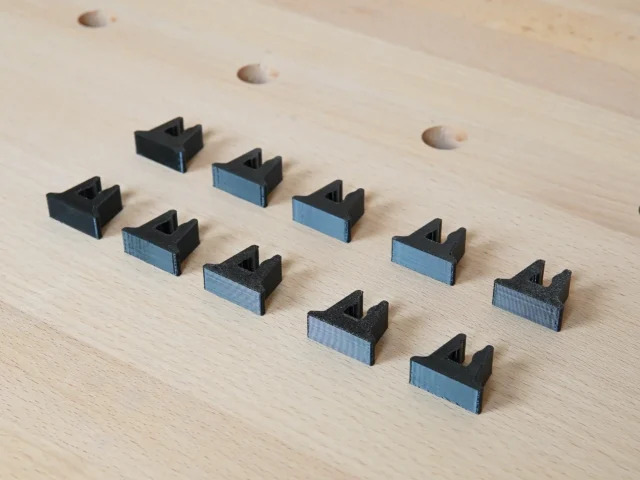 Ten black and blue 3D-printed stop blocks arranged on a light wood surface with pocket holes visible above