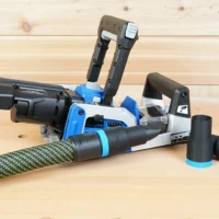 Black ToolCurve hose adapter with blue band joining a vacuum hose to a Kreg Rebel pocket hole joiner, two spare adapters beside it