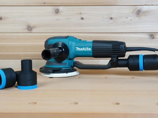Black ToolCurve 36mm hose adapter with blue ring installed on a Makita random orbit sander, spare shown beside