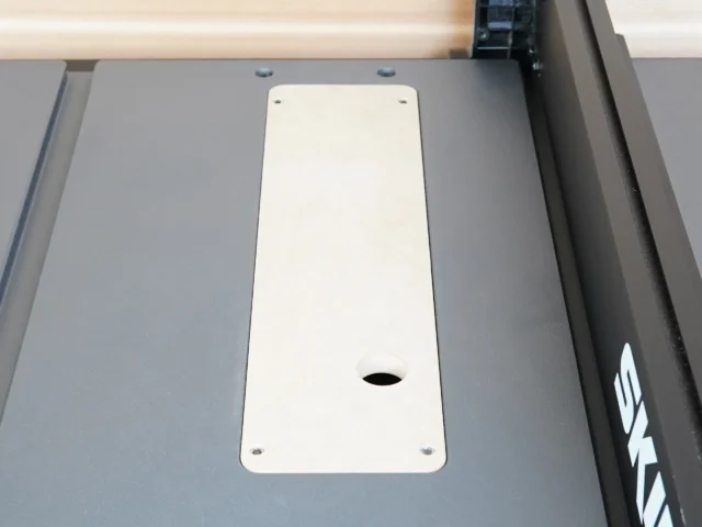 White zero clearance insert mounted in gray table saw top with four screw holes and center blade opening