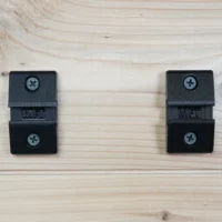 Pair of black MFT wall-mounts with Phillips head screws, shown on light wood surface