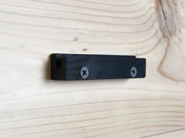 Black wall mount holder with screw holes for attaching a track saw guide rail square to shop wall or cabinet