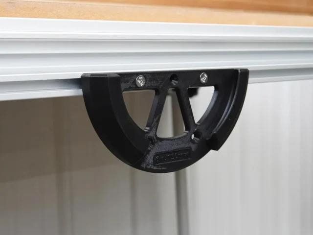 Black sander holder mounted to Festool MFT/3 table's T-track rail, showing open cradle design with mounting screws visible