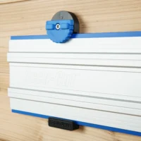 Blue wall mount clamp gripping a Kreg Accu-Cut track saw rail mounted on wood, showing locking mechanism and gripper pads