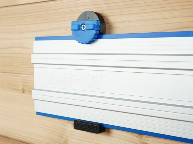Blue wall mount clamp gripping a Kreg Accu-Cut track saw rail mounted on wood, showing locking mechanism and gripper pads