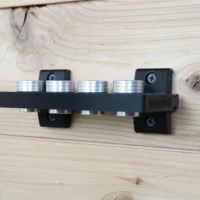 Two black ToolCurve wall-mount brackets screwed to a wood wall, holding a rail with four magnet stacks