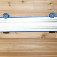 Wall mount for Kreg Accu-Cut track saw rail with blue end clamps and locking handles, mounted on wooden wall