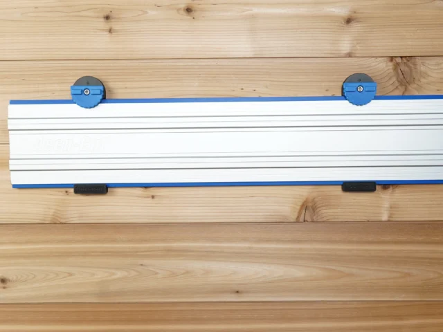 Wall mount for Kreg Accu-Cut track saw rail with blue end clamps and locking handles, mounted on wooden wall