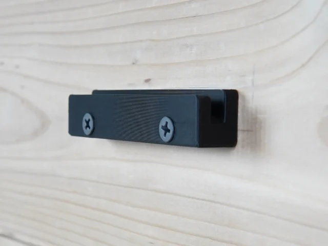Dark blue wall mount with two Phillips screw holes, mounted horizontally on light wood
