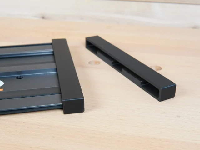 Two black protective caps for Ridgid track saw rails, one attached to the rail and one displayed separately on wood surface