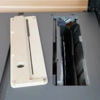 White MDF zero clearance insert next to its rectangular opening in a SKIL table saw top, showing mounting holes and dust port.