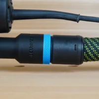 Black hose adapter with blue band attached to Makita random orbit sander, connected to green-and-black braided dust hose