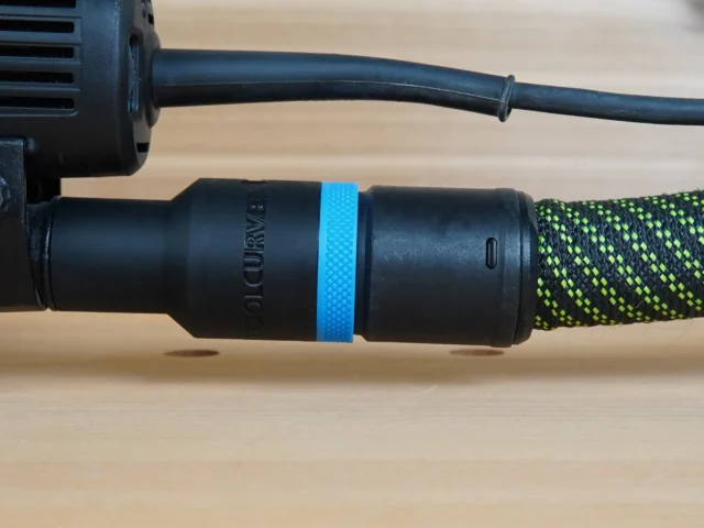 Black hose adapter with blue band attached to Makita random orbit sander, connected to green-and-black braided dust hose