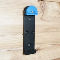 Black wall mount with blue top clamp attached to wooden wall, showing three mounting holes and ToolCurve branding