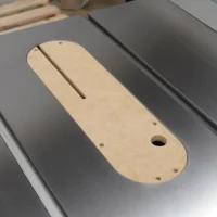 Light wood MDF zero clearance insert with rounded ends, center slot, and mounting holes, positioned on a gray table saw insert opening