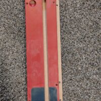 Red and natural wood zero clearance insert with central slot, circular port, and dark toe piece, shown flat.
