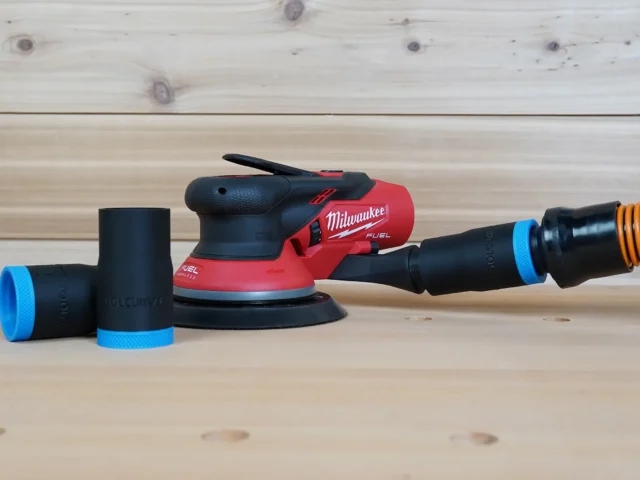 Black 1-1/4" hose adapter with blue trim linking an orange hose to a Milwaukee M12 sander, spare parts beside