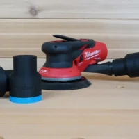 Black ToolCurve 1-7/8 inch hose adapter with blue collar beside a Milwaukee M12 random orbit sander