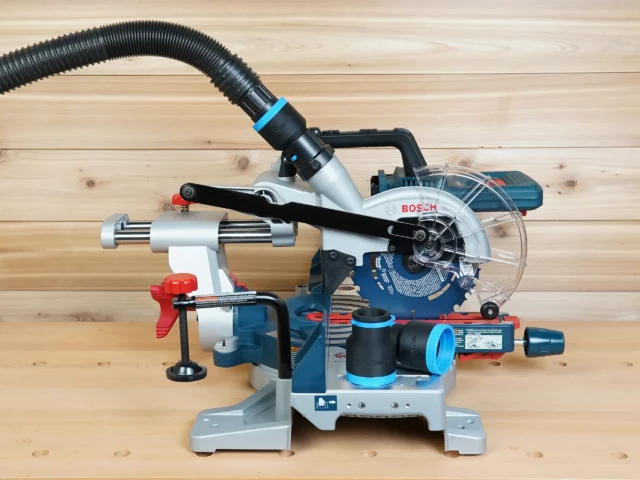 Black and blue ToolCurve 1-7/8 inch hose adapter joining a vacuum hose to a Bosch 18v miter saw dust port, with a second adapter resting on the saw base