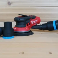 Black and blue 36mm hose adapter connecting a vacuum hose to a Milwaukee M12 Fuel sander, with two spare adapters beside it