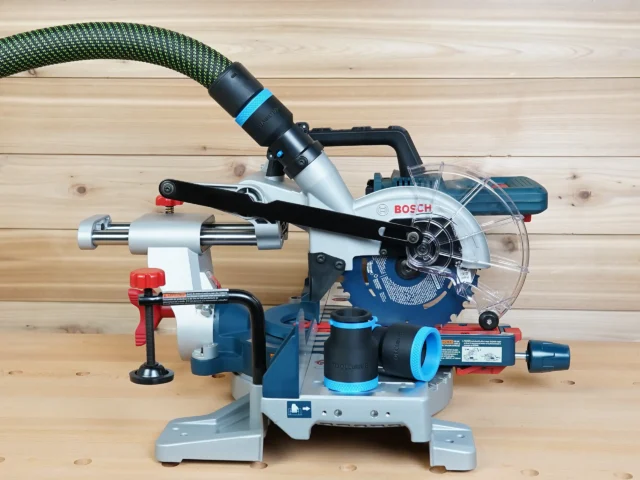 Black 36mm hose adapter with blue accents on a Bosch 18v miter saw dust port, extractor hose attached, second adapter resting on the base