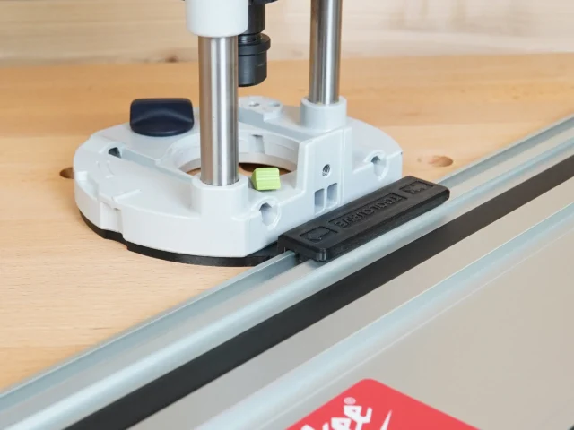 White plastic guide rail adapter mounted on Festool 1400 router, attached to aluminum guide rail on workbench