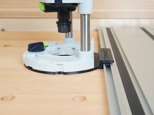 White guide rail adapter mounted on Festool 1400 router, positioned against Festool track saw rail on wood workbench