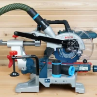 Black and blue ToolCurve hose adapter fitted to a Bosch 18v miter saw dust port with extractor hose attached, plus two spare adapters on the base