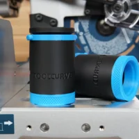 Two black hose adapters with blue grip rings, displayed separately on a gray platform in a workshop setting