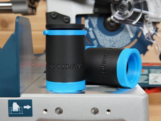 Two black hose adapters with blue grip rings, displayed separately on a gray platform in a workshop setting