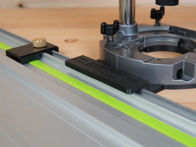 Black adapter mounted on Festool guide rail, connected to Makita router base with brass leveling knob visible on left