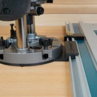 Guide Rail Adapter for Makita router mounted on a Makita track saw, showing the gray aluminum base plate clamped to the rail with the router positioned above