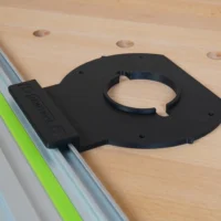 Black adapter mounted on Festool-style guide rail, with circular ring opening for router attachment and mounting holes visible