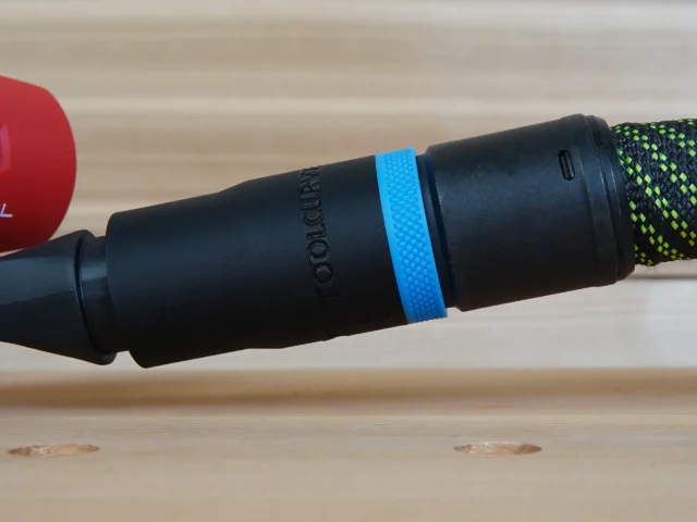 Black hose adapter with blue band attached to Milwaukee sander dust port, showing threaded connection and braided hose on right
