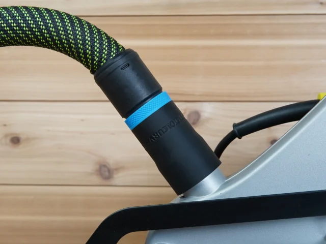 Black hose adapter with blue band attached to Ryobi compound miter saw dust port, with green and yellow braided hose connected above