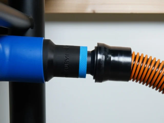 Black ToolCurve 1-1/4 inch hose adapter with blue band joining a Delta table saw port to an orange vac hose