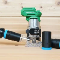 Black 1-1/4 inch hose adapter with blue collar joining an orange vac hose to a Metabo HPT trim router, with two spare adapters
