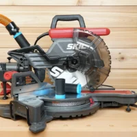 Black 1-1/4" hose adapter with blue collar on a SKIL 10-inch miter saw, second adapter linking orange hose