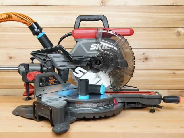 Black 1-1/4" hose adapter with blue collar on a SKIL 10-inch miter saw, second adapter linking orange hose