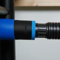 Black 1-7/8 inch ToolCurve hose adapter with blue collar joining a ribbed vacuum hose to a Delta table saw dust port