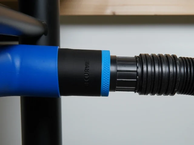 Black 1-7/8 inch ToolCurve hose adapter with blue collar joining a ribbed vacuum hose to a Delta table saw dust port