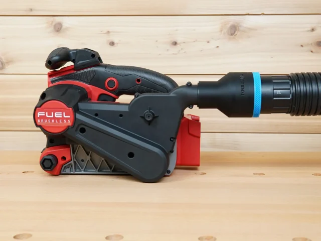 Black ToolCurve 2-1/2 inch hose adapter with blue ring joining a vacuum hose to a Milwaukee M18 belt sander dust port