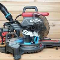Two black ToolCurve 2-1/2 inch hose adapters with blue rings resting on a SKIL 10 inch miter saw table, one attached to a hose